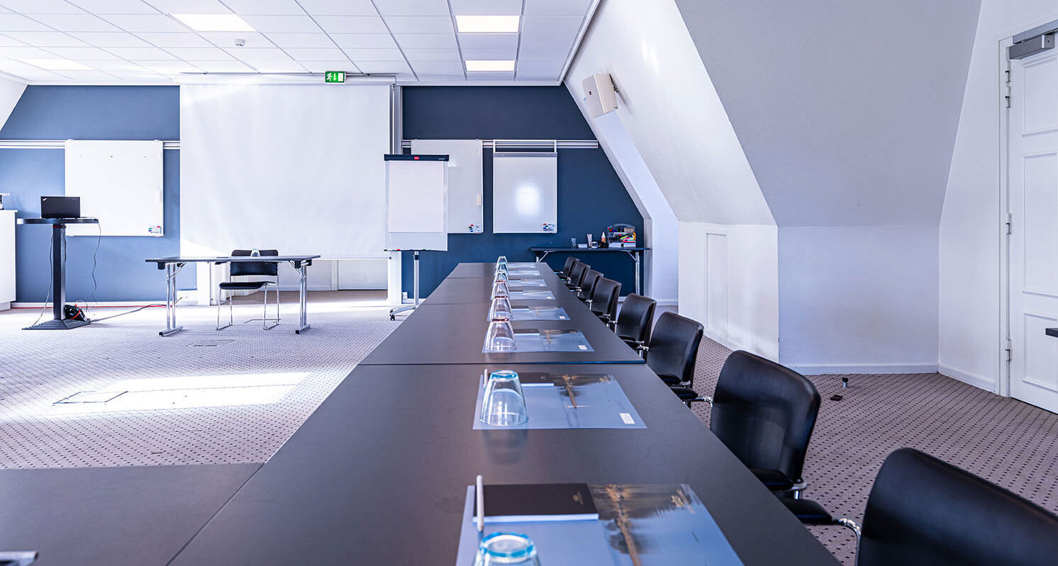 Konferencelokale med tavler, flipover og et langt bord langs væggen 