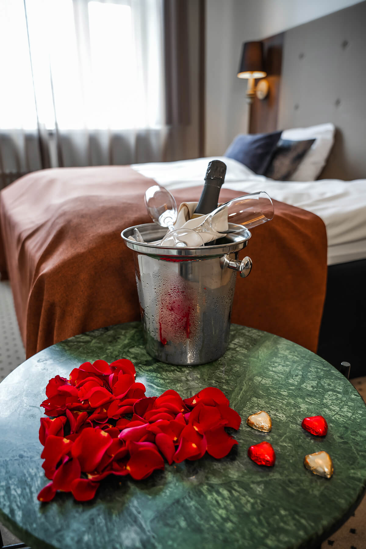 Et hotelværelse hvor der foran sengen står et bord med vinkøler og rosenblade