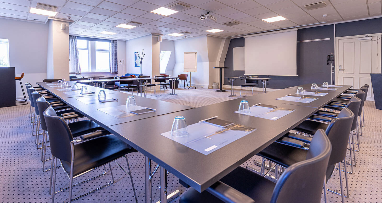 Konferencelokale med borde i u-form, tavler og lysindfald fra vindue