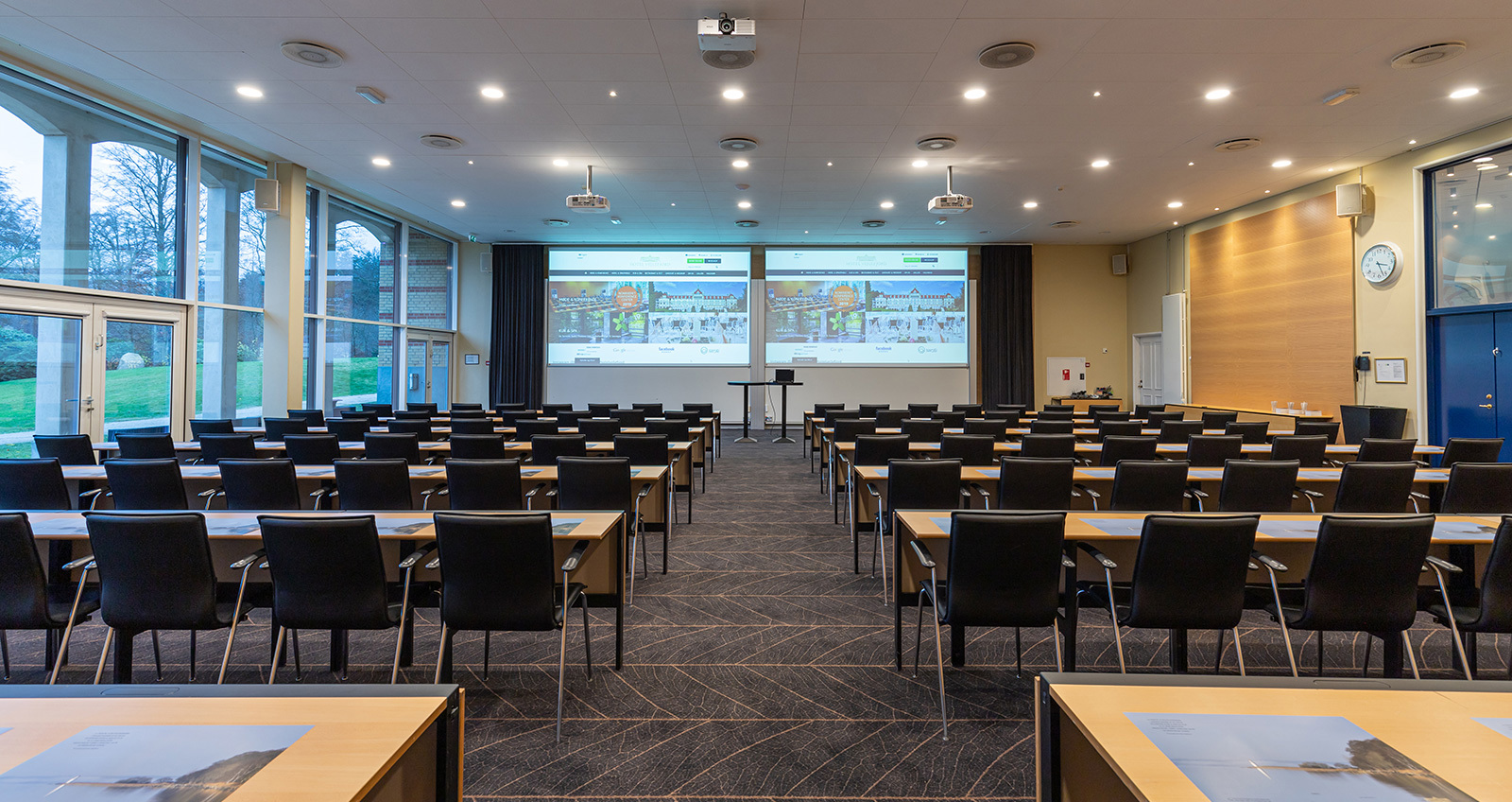 Konferencelokale med stole og borde opstillet mod to lærreder