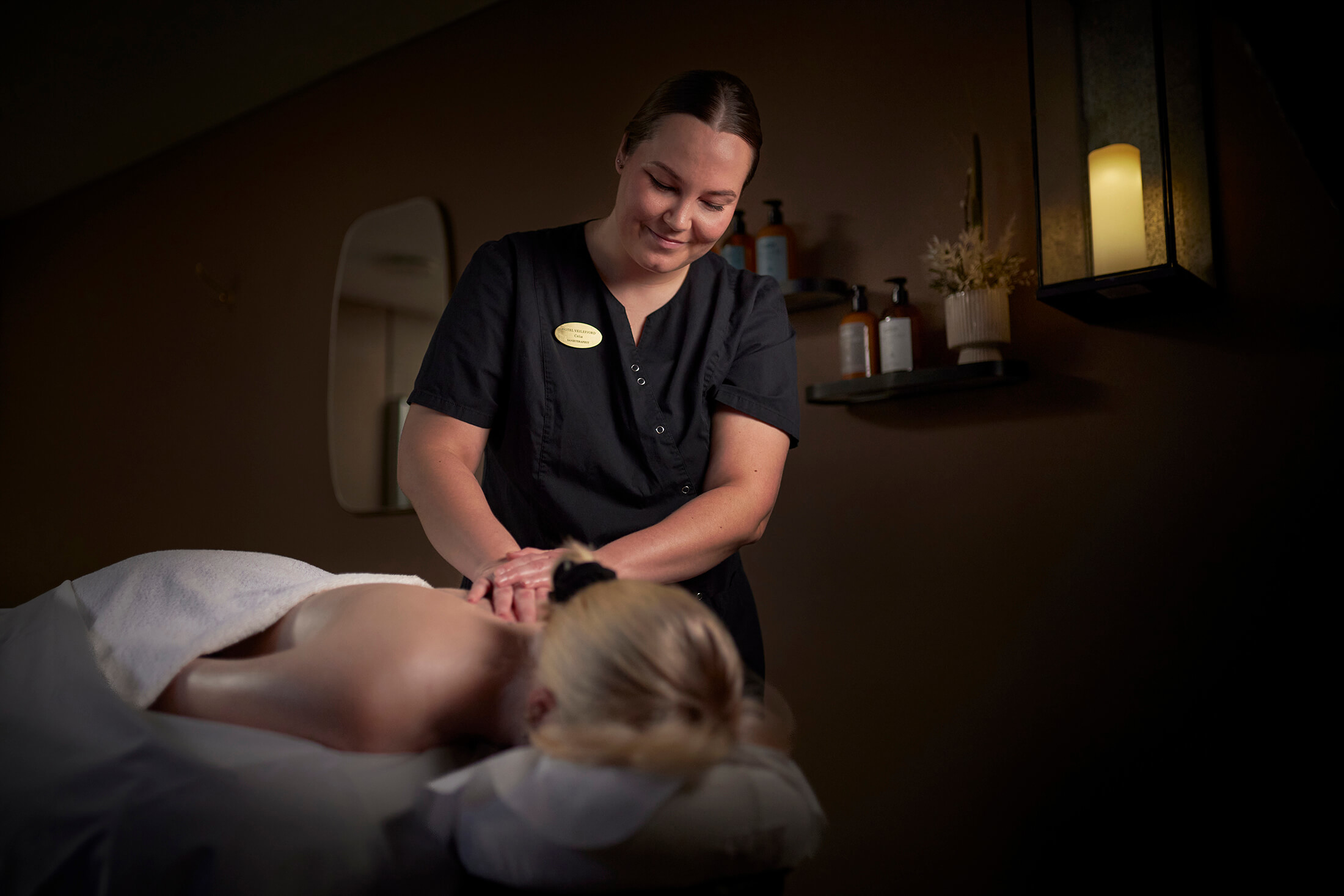 En kvinde er ved at få massage i et hyggeligt rum med levende lys