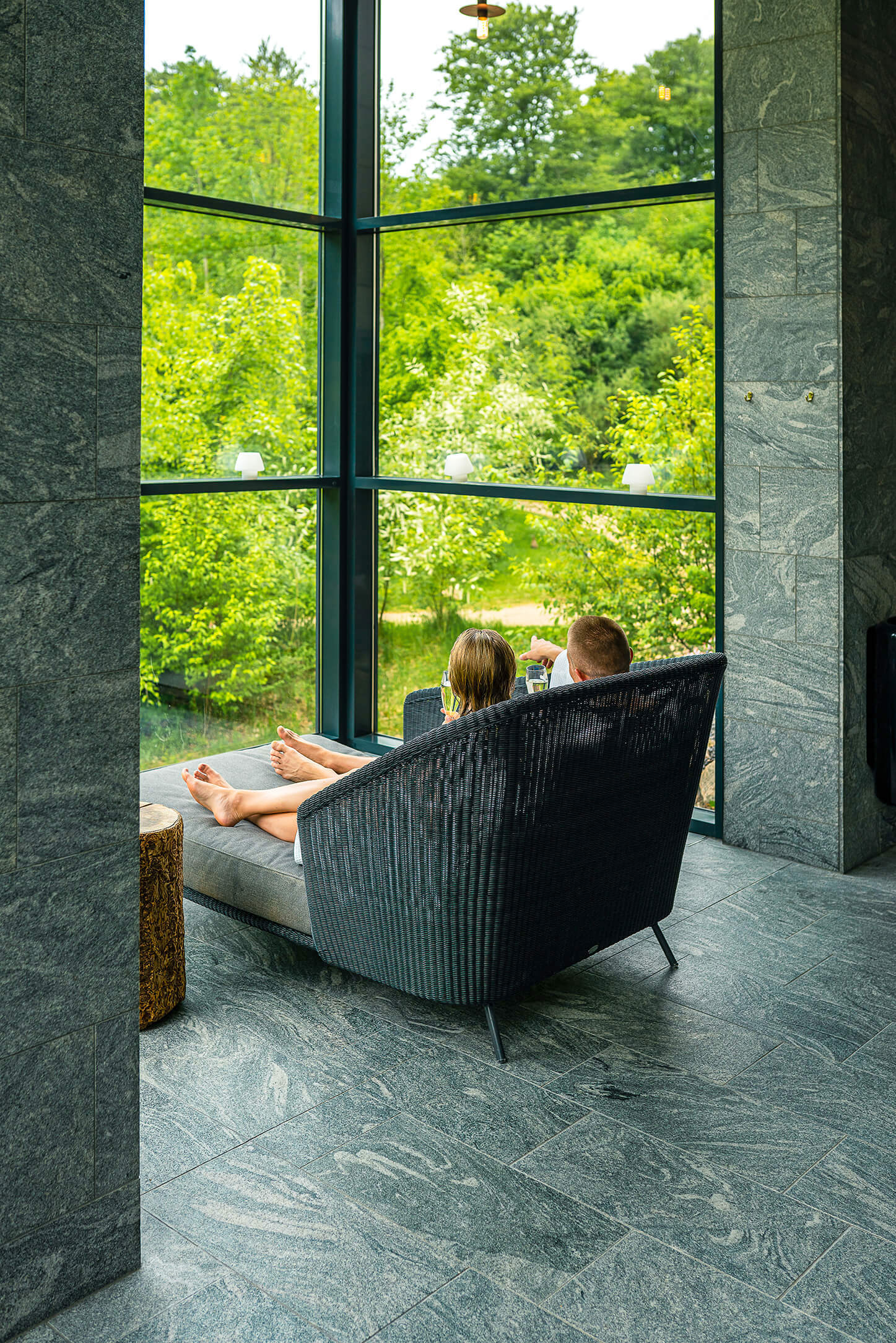 Et par sidder i en loungestol foran et stort vindue der inviterer naturen indenfor i spa