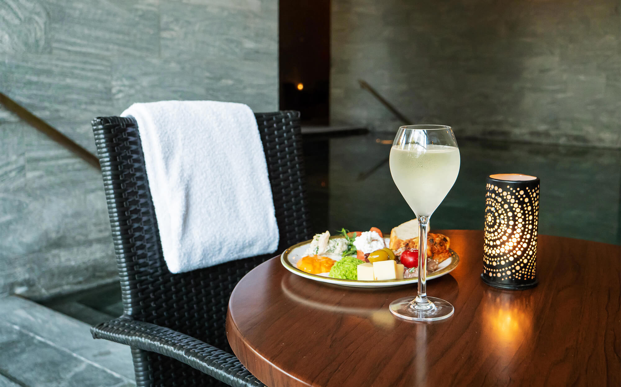 Et cafebord dækket op med en drink og frugt i en spa med bassin i baggrunden