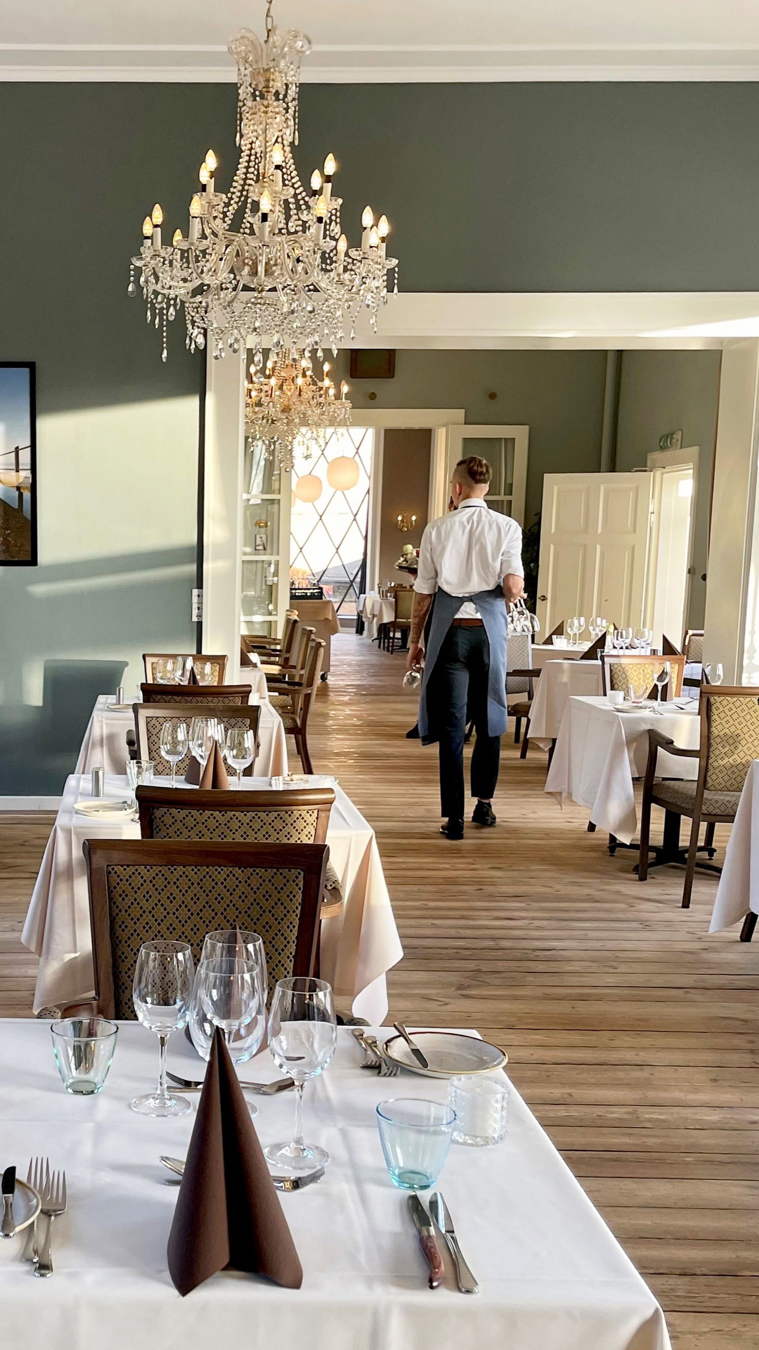 Et bord i en restaurant dækket op til middag, hvor to stole kigger ud på en parks flotte udsigt