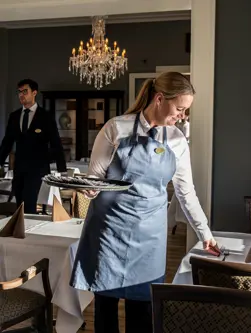 En tjener går med et fad og dækker bordene op til fest i en flot restaurant med lysekrone