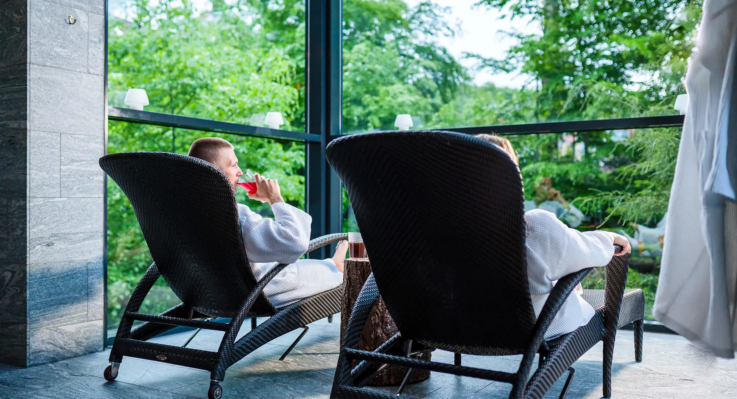 Et par i badkåber slapper af i liggestole i en spa omgivet af natur