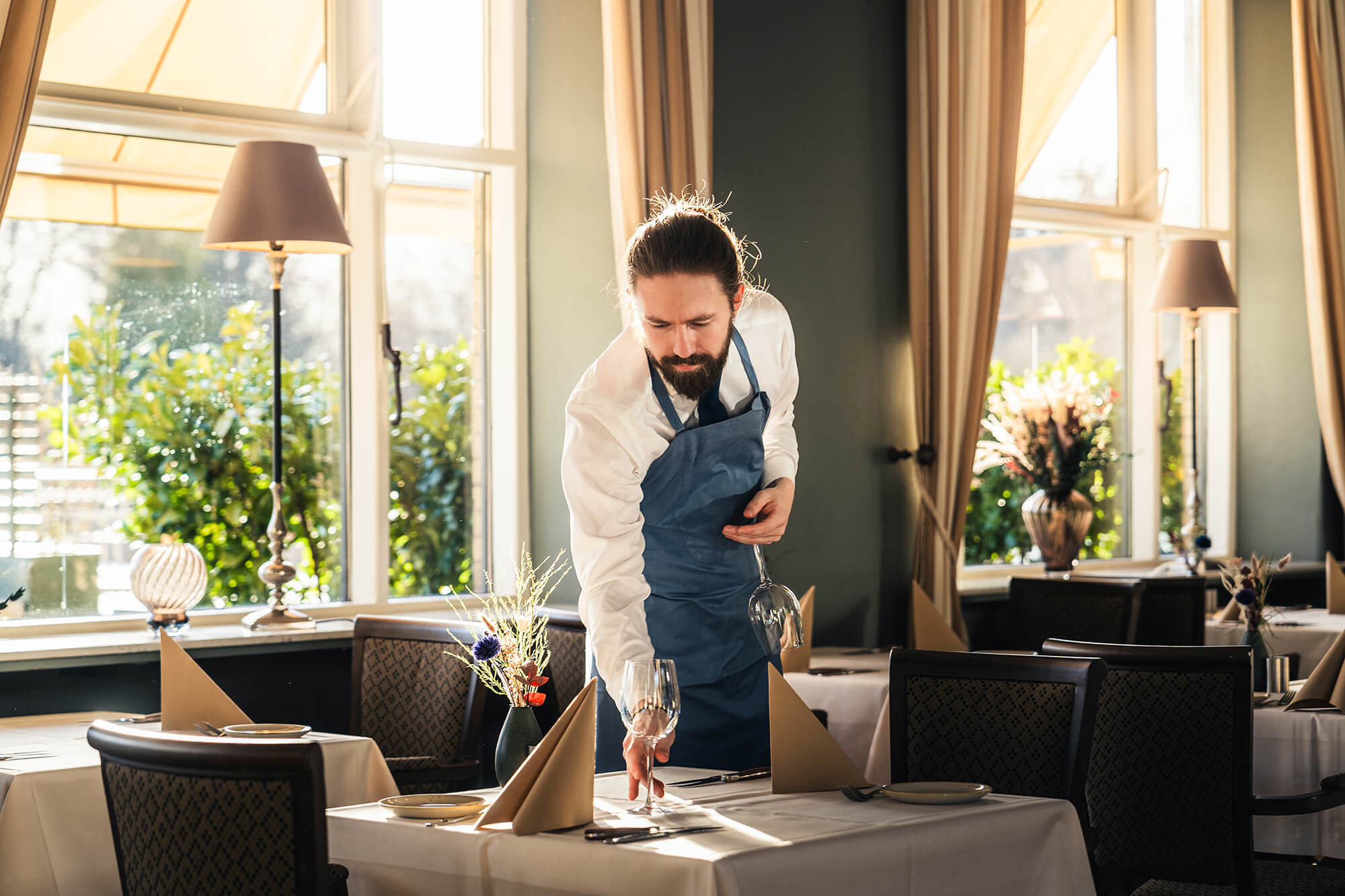En tjener er ved at dække bord i en hyggelig restaurant
